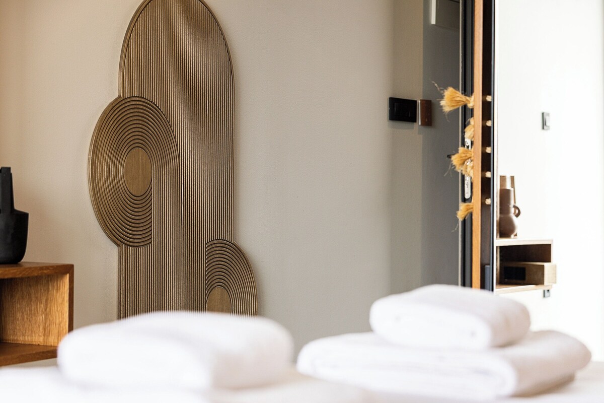 A modern room with a large mirror, wooden wall art, and a wooden side table.