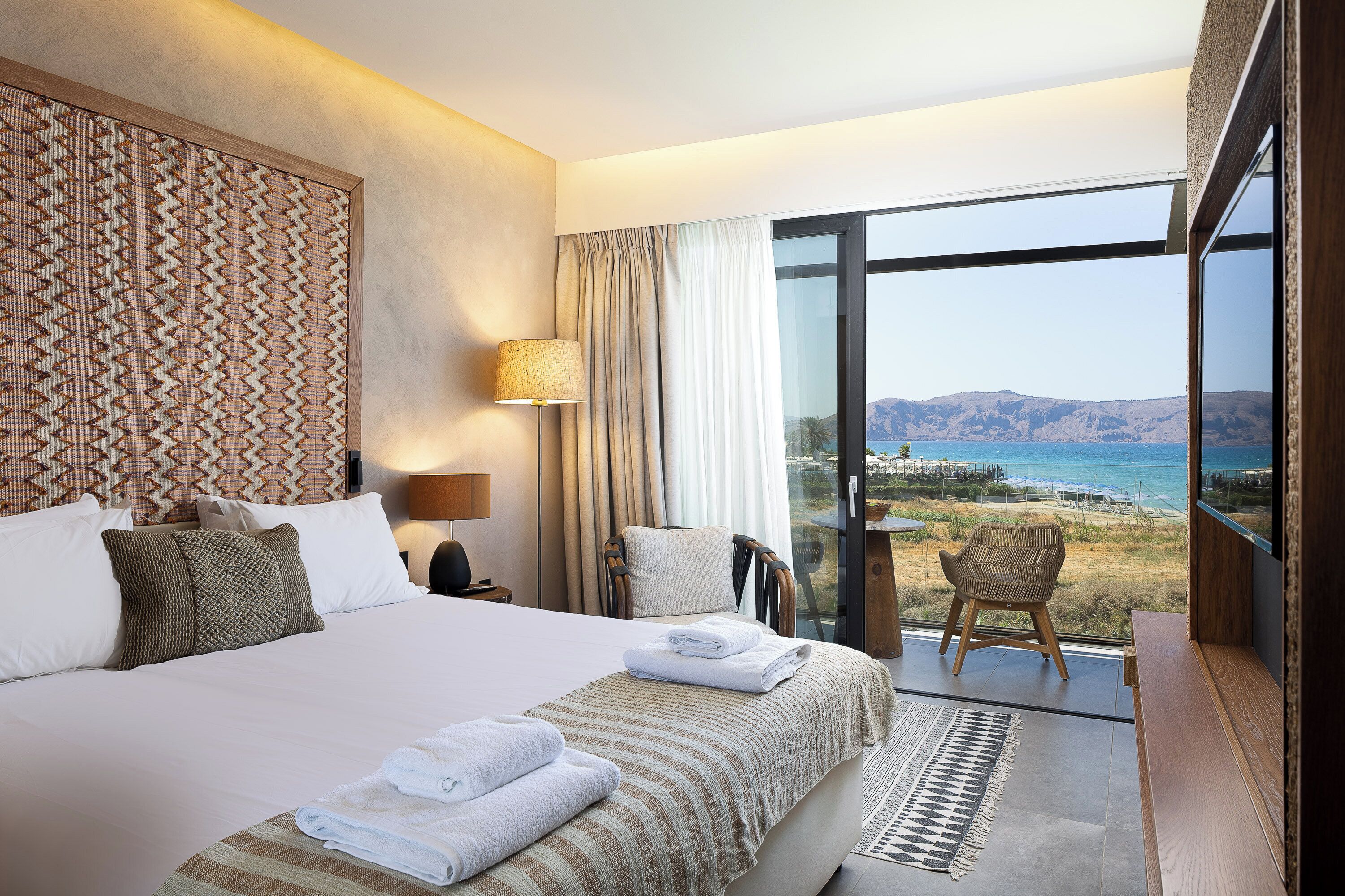 Une chambre d’hôtel avec un grand lit, une vue sur la mer et un balcon avec une chaise.