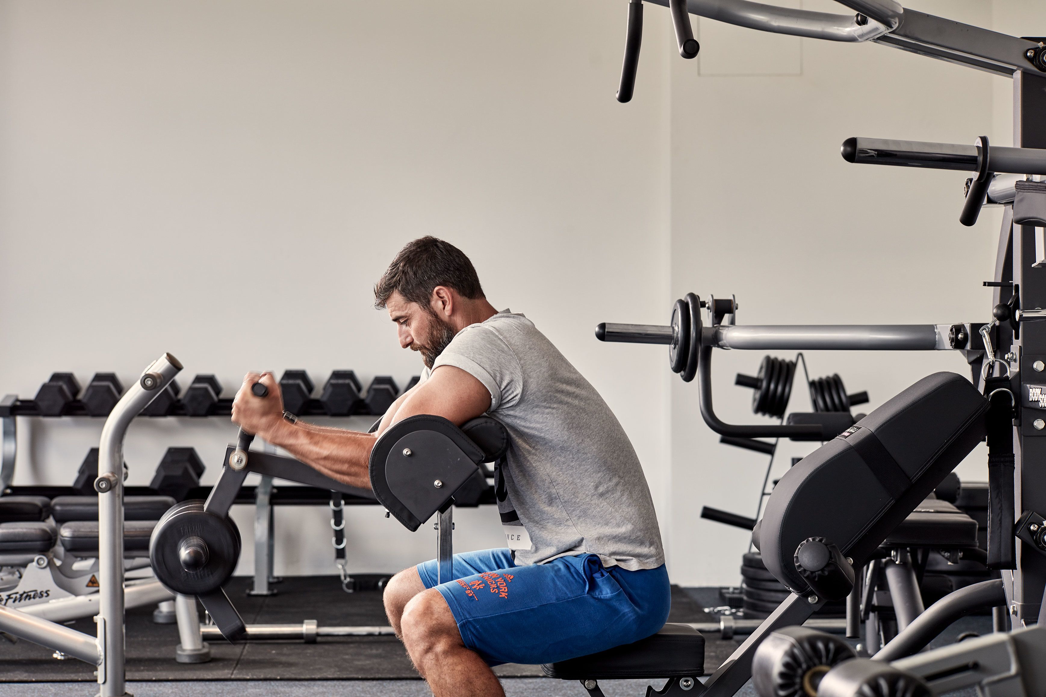 A man using a seated chest press machine in a gym with dumbbells and other equipment in the background.