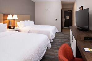 A hotel room with two beds, a desk with a TV, a lamp, and a red chair.
