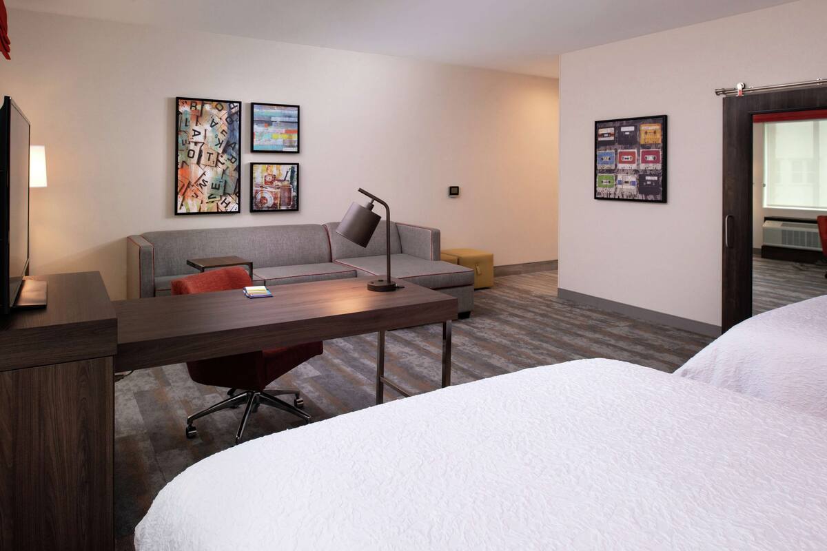 Une chambre d’hôtel comprenant un lit, un bureau, une chaise, un canapé et des œuvres d’art accrochées aux murs.