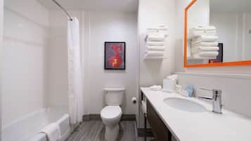 A modern bathroom with a bathtub, toilet, and sink. There is a framed artwork on the wall and a stack of towels on the wall.