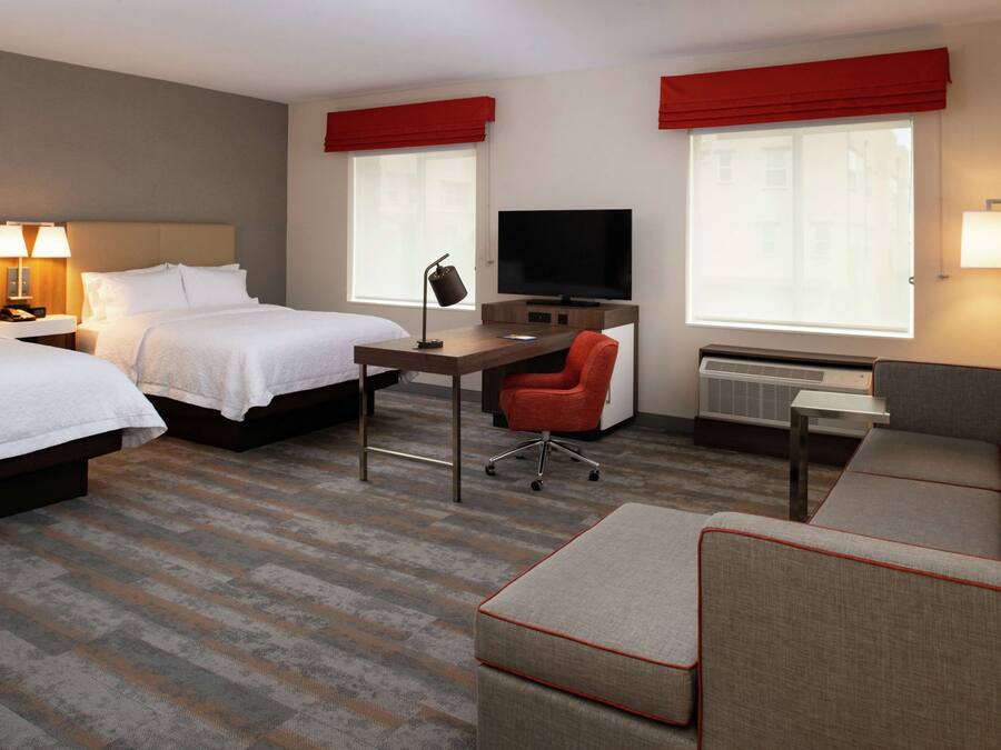 A hotel room with two beds, a desk with a chair, a television, and a sofa.