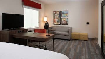 A hotel room with a bed, a desk with a TV, a sofa, a lamp, and two storage boxes.