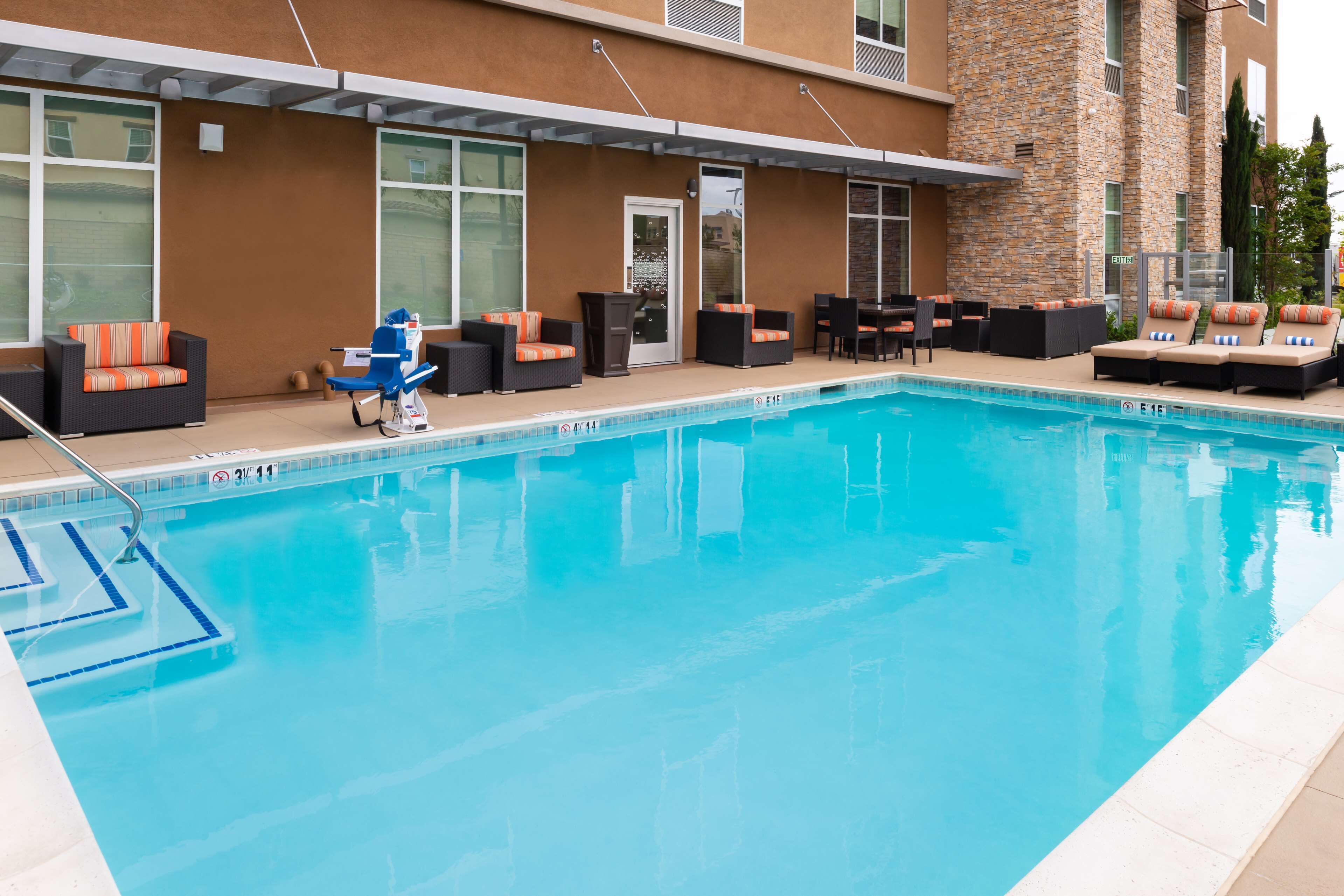 Una piscina con sillones y mesas, un área de patio techada y la fachada de un edificio de piedra.