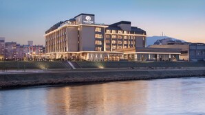 A modern hotel with a prominent entrance, multiple floors, and a waterfront view. - DoubleTree by Hilton Skopje (Skopje)