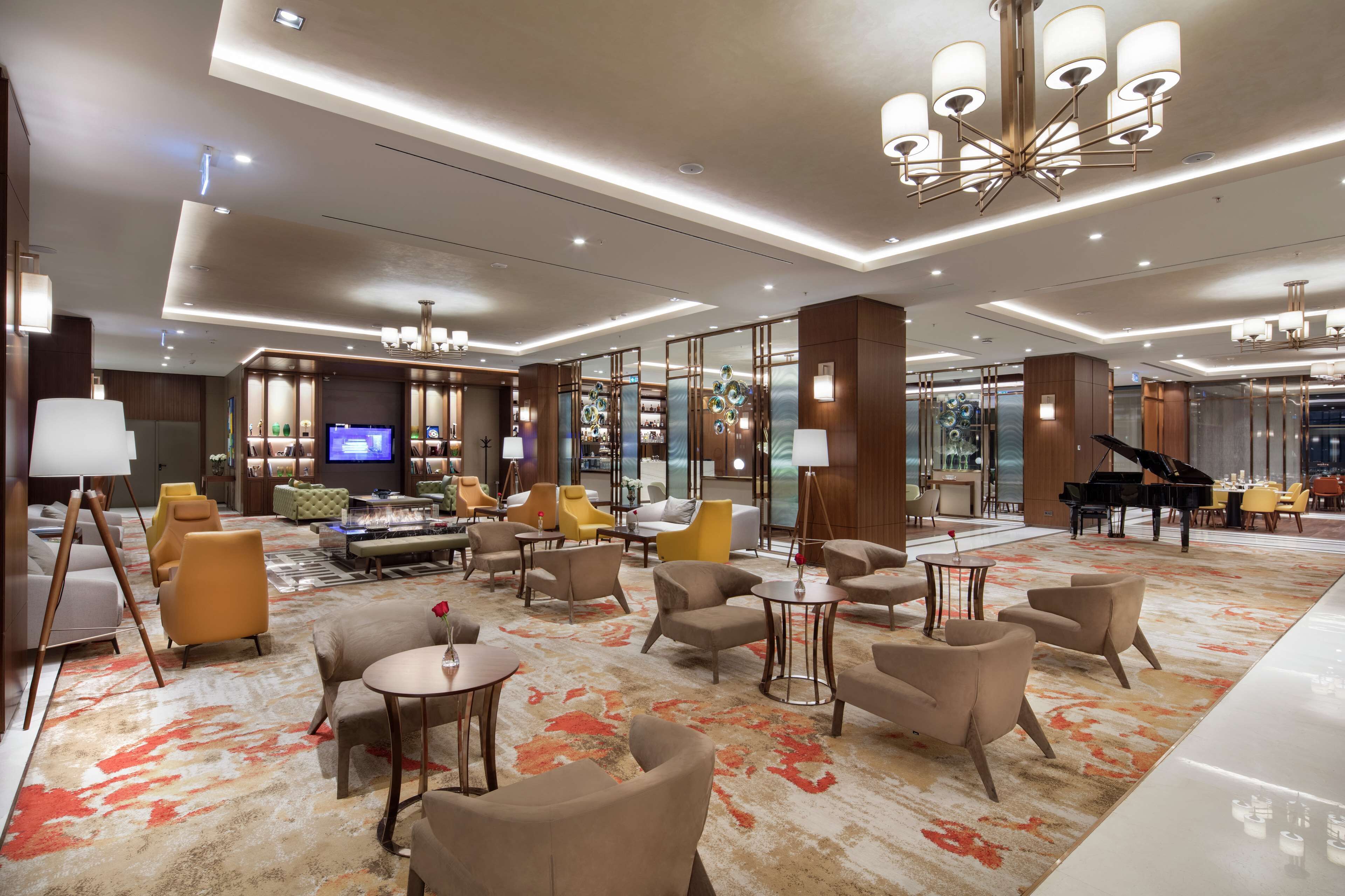 A spacious lobby with modern furnishings, a grand piano, and a large chandelier.