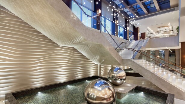 A modern indoor pool area with a unique wavy wall design, a glass-bottomed pool, and a staircase leading to upper levels. - DoubleTree by Hilton Skopje (Skopje)