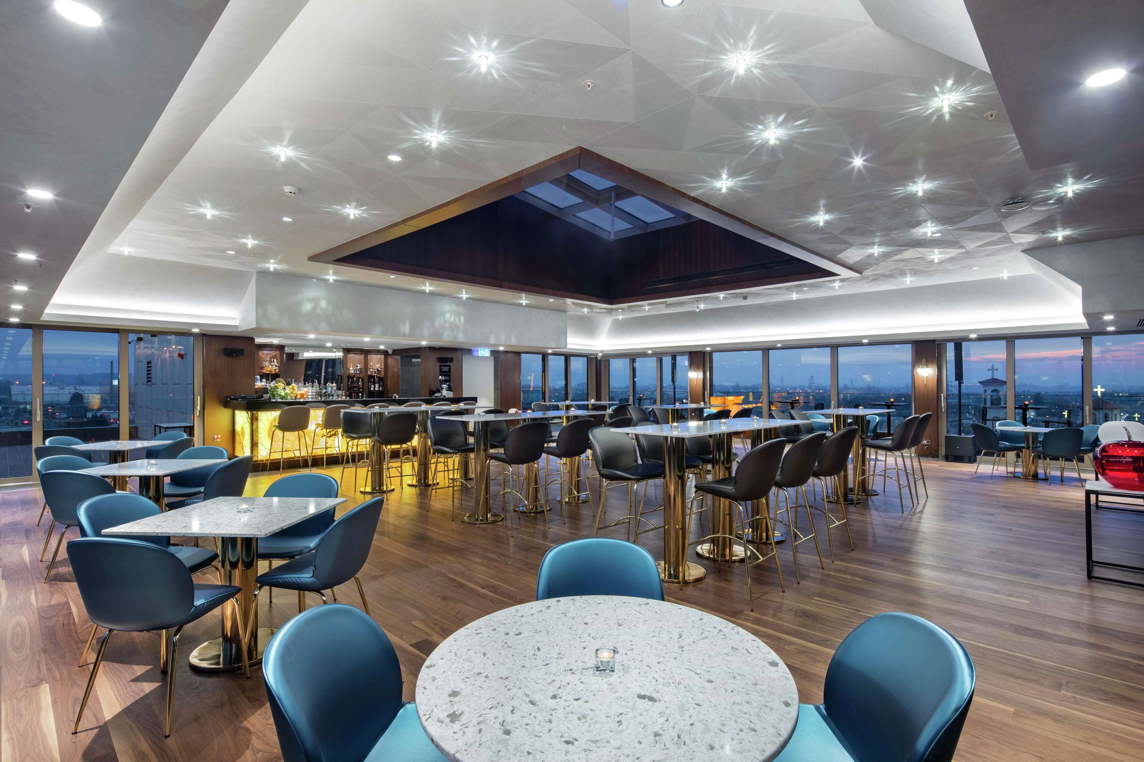 A modern restaurant with a high ceiling, large windows, and a bar area.