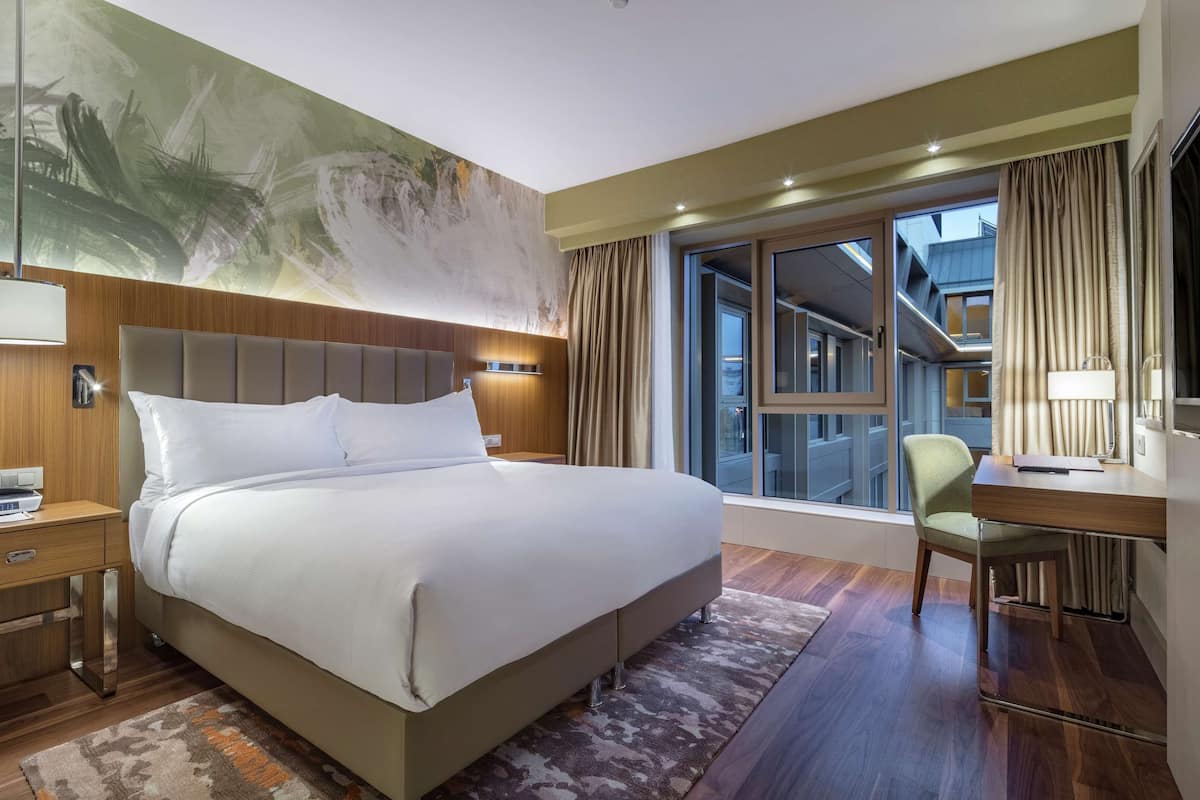 A modern hotel room with a large bed, a desk, and a TV.