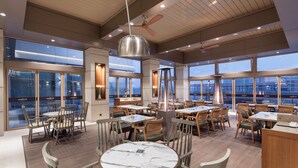 A modern restaurant with round tables and chairs, large windows, and a view of the city. - DoubleTree by Hilton Skopje (Skopje)
