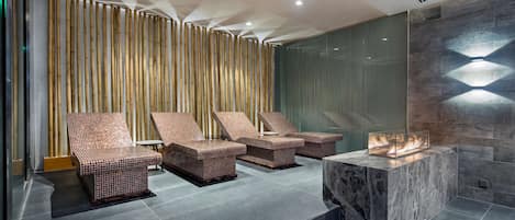 A modern spa area with three wicker lounge chairs, a marble bench, and a built-in fire feature.
