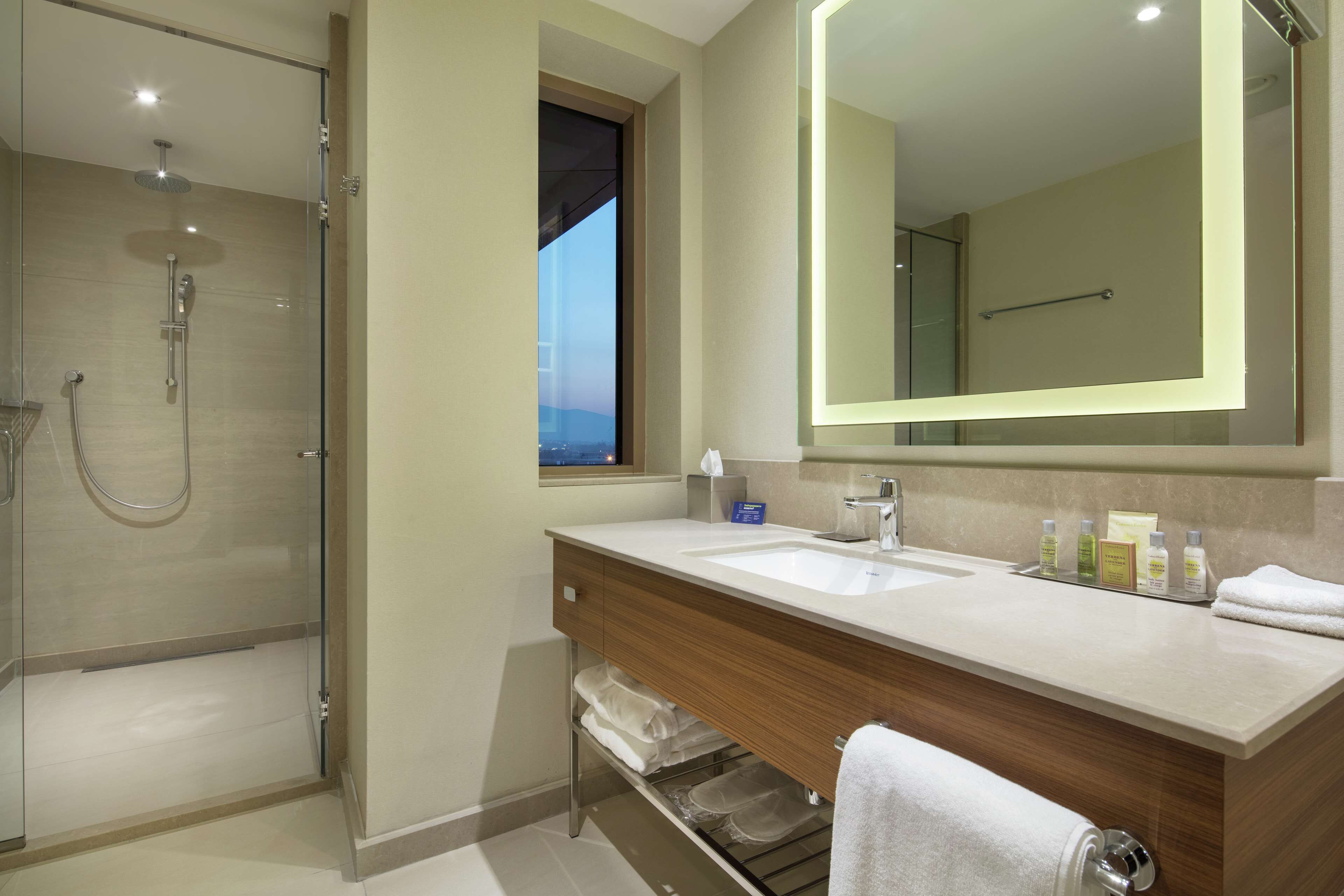 Un bagno moderno con cabina doccia in vetro, uno specchio grande e un mobile lavabo con lavandino e spazio contenitore.