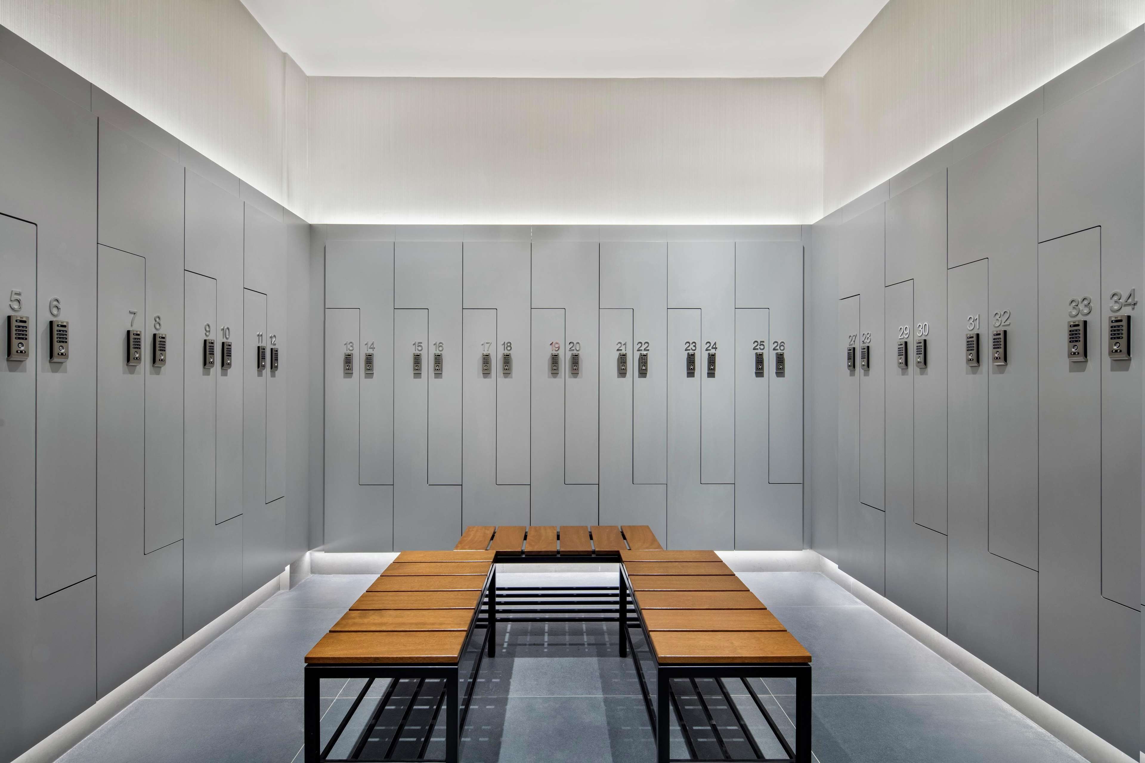Un vestiaire moderne et minimaliste, doté de casiers numérotés et d’un banc central en bois.