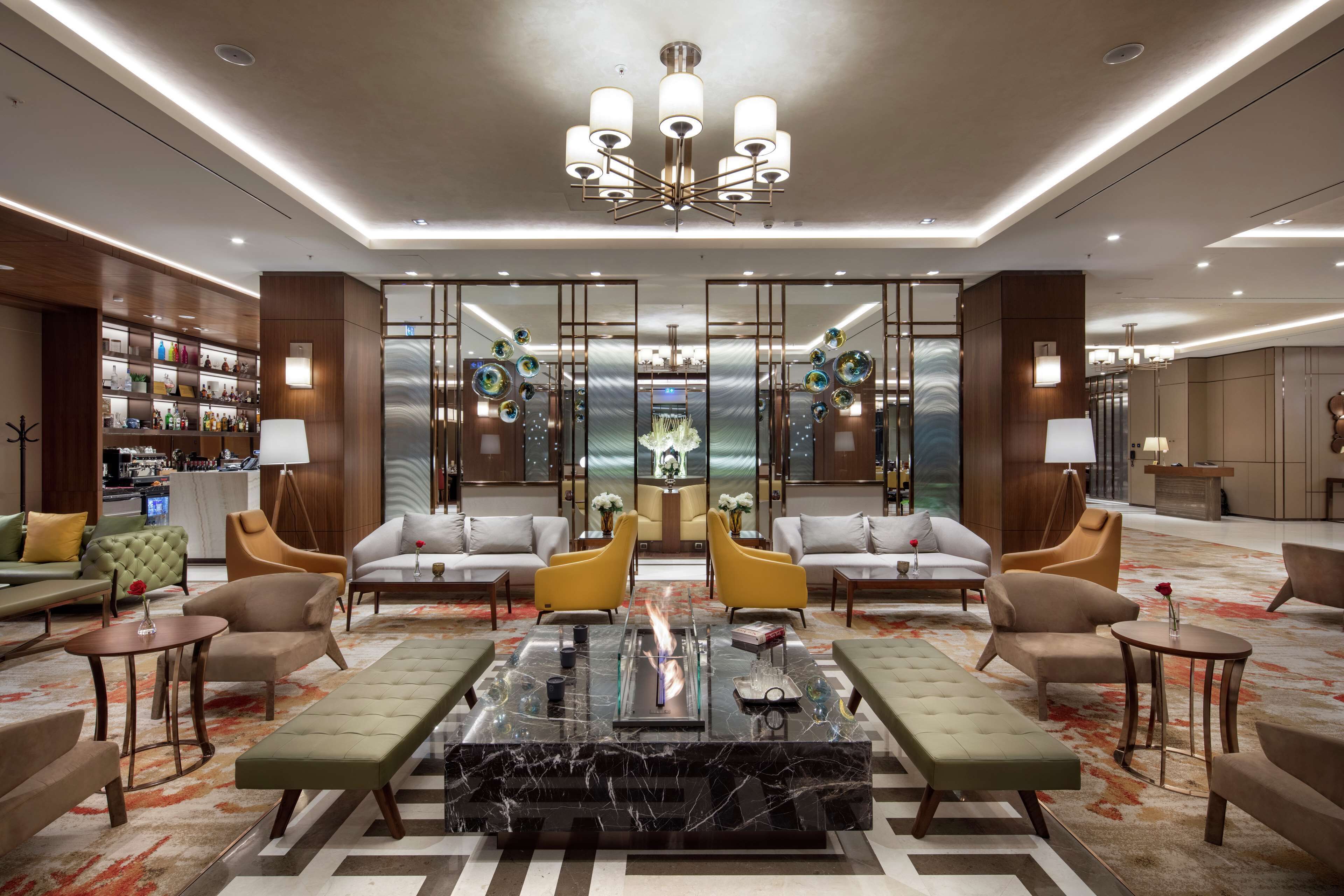 A spacious lobby with a central seating area, a chandelier, and a bar with shelves of bottles.