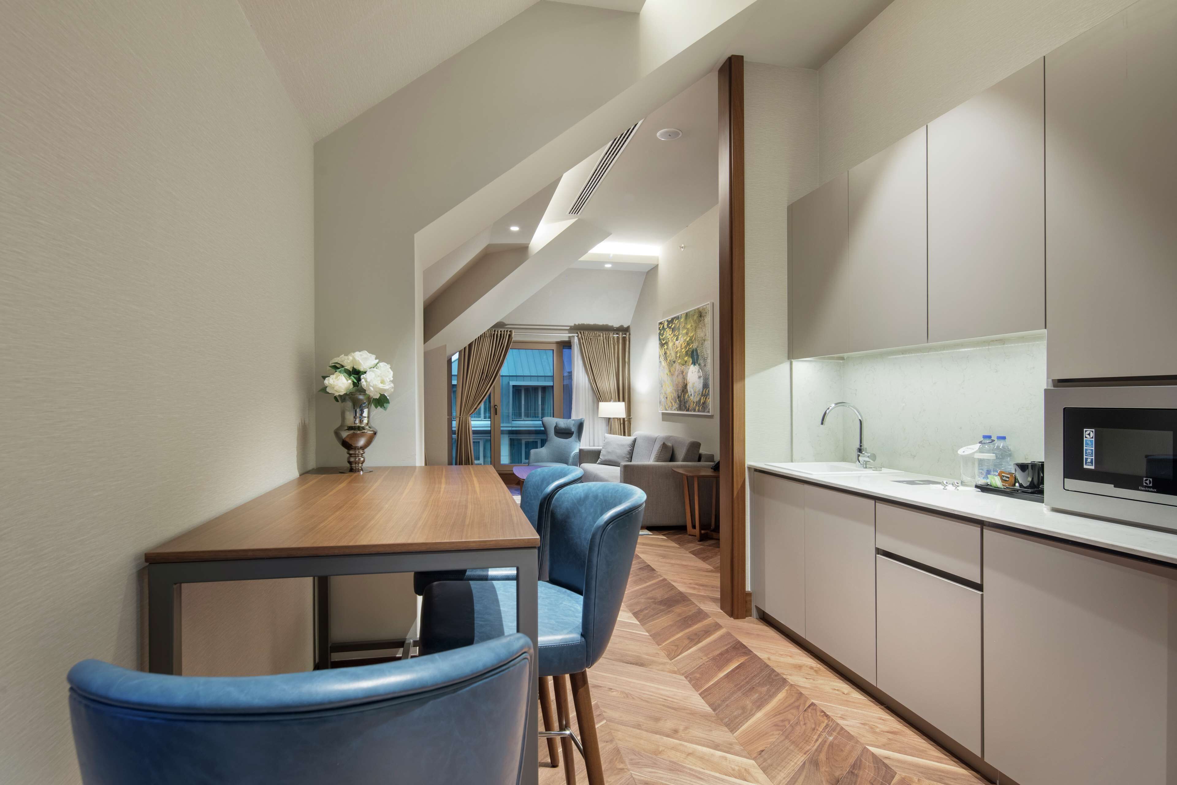 Une cuisine moderne avec un parquet en bois disposé en chevrons, un coin repas avec des chaises bleues et une vue sur un balcon.