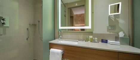 A modern bathroom with a glass shower enclosure, a large mirror, a sink with toiletries, and a towel rack.