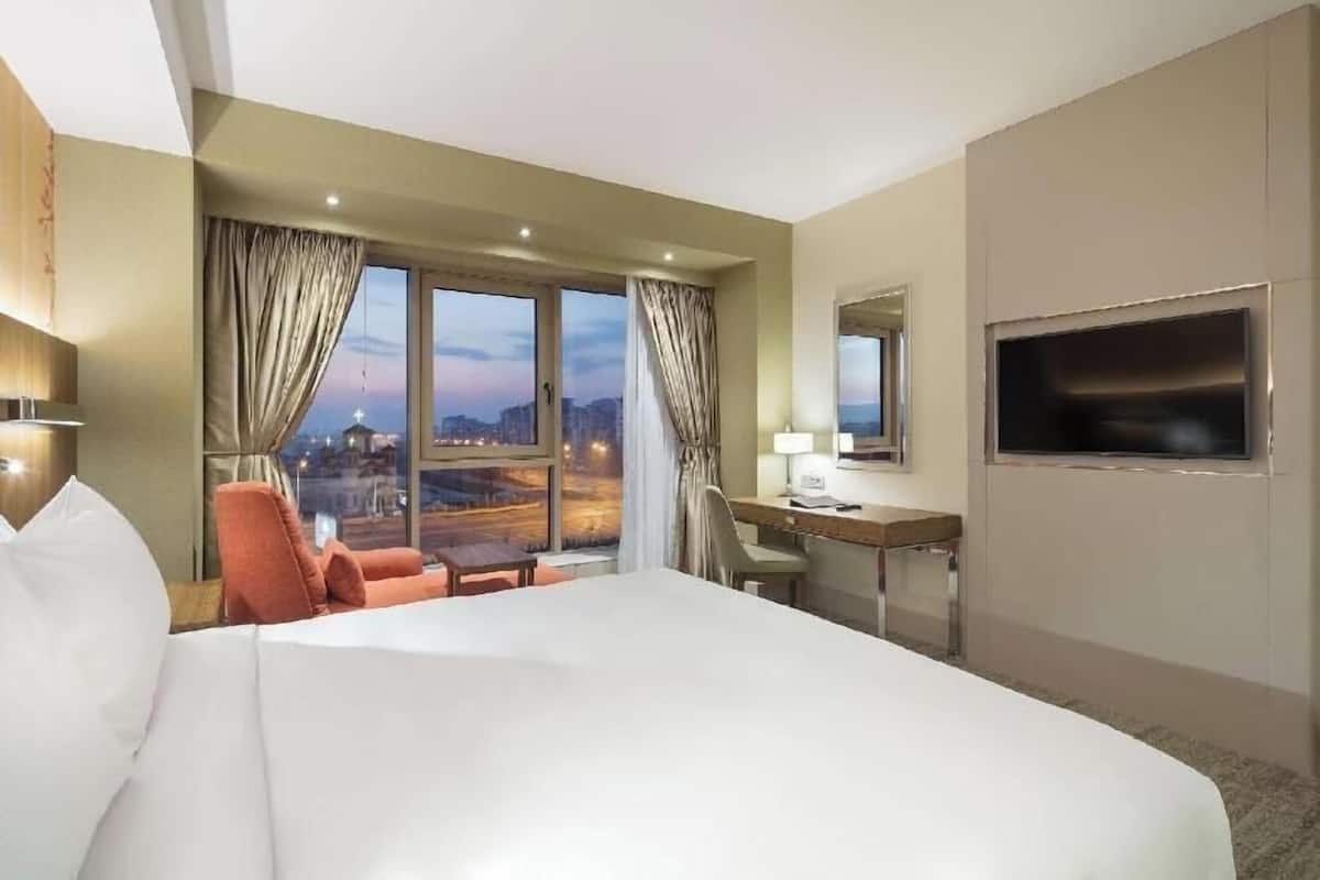 A hotel room with a large bed, a desk, a chair, and a TV.