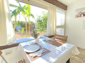 A dining area with a table set for two, a potted plant, and a view of a garden with banana trees. - B&B Fellini (Gallipoli)