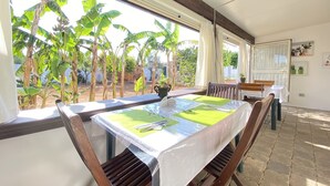 A dining area with a table set for two, large windows with a view of banana trees, and a wooden ceiling. - B&B Fellini (Gallipoli)