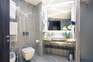 A modern bathroom with a marble wall, a toilet, a sink with a mirror, and a trash bin.