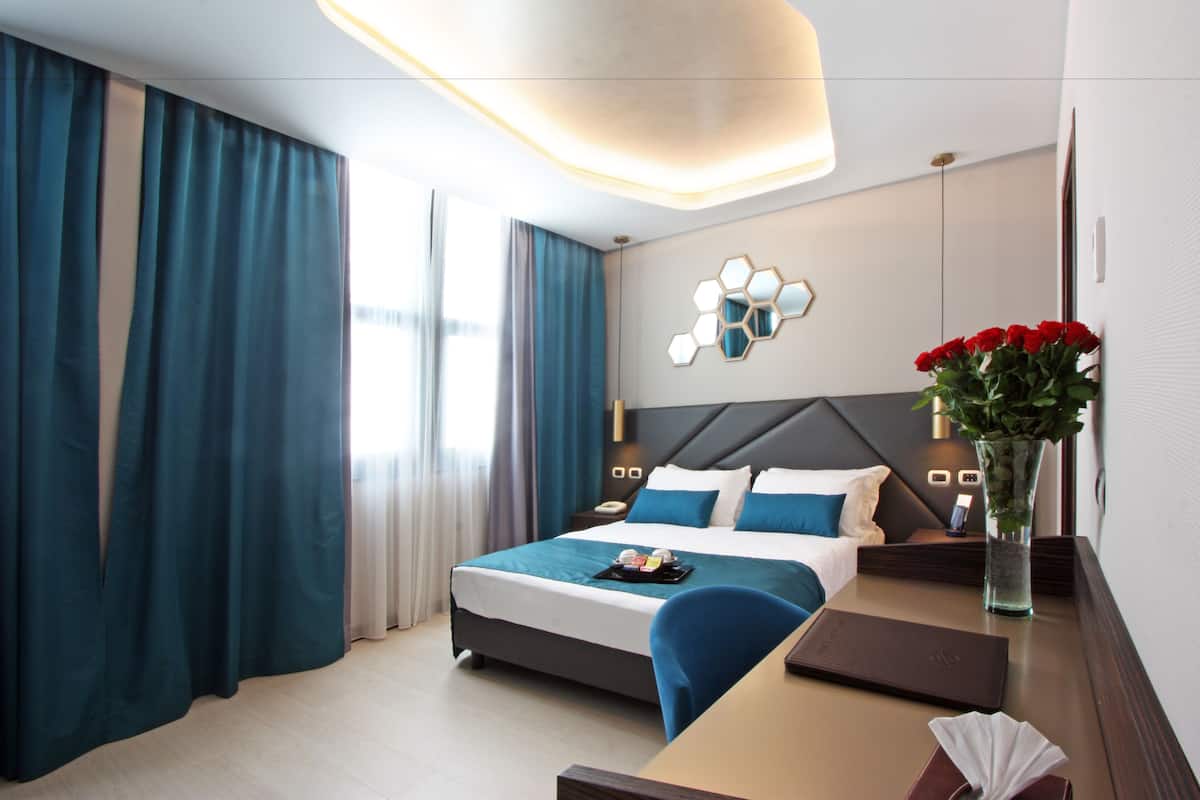 A modern hotel room with a large bed, a desk, and a vase of flowers.
