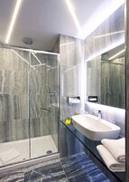 A modern bathroom with a glass shower enclosure, a white sink, and a large mirror.