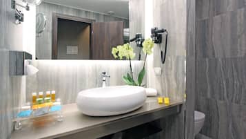A modern bathroom with a large oval sink, a mirror, and a hairdryer mounted on the wall.