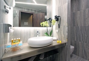 A modern bathroom with a large oval sink, a mirror, and a hairdryer mounted on the wall.