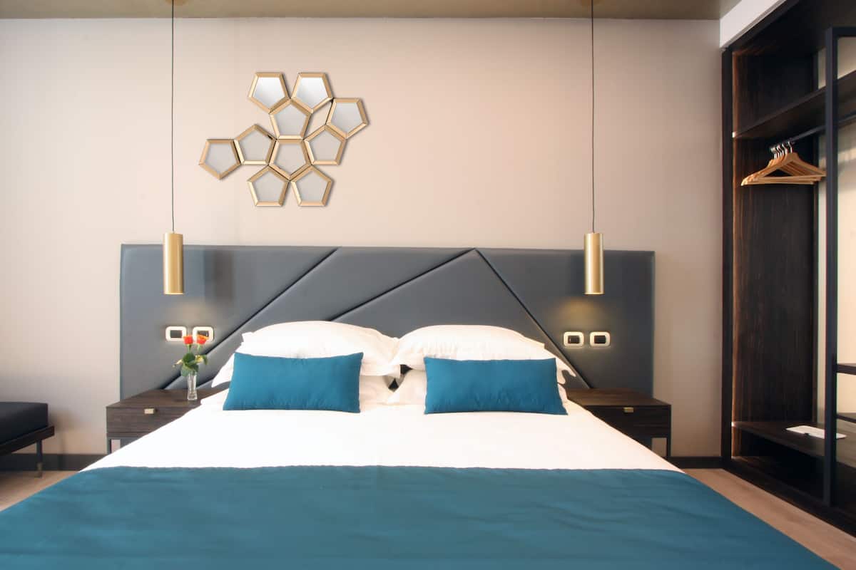 A modern bedroom with a large bed, two bedside tables, a wall-mounted light fixture, and a wardrobe.