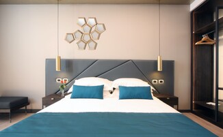 A modern bedroom with a large bed, two bedside tables, a wall-mounted light fixture, and a wardrobe.