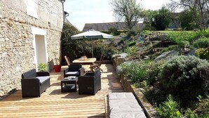 Una terraza de madera con mobiliario exterior, una mesa y una sombrilla.