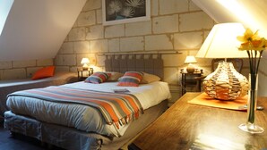 Un dormitorio acogedor con techo inclinado, una cama grande con ropa de cama a rayas, dos lámparas de noche y una lámpara decorativa de fibra en la mesita.