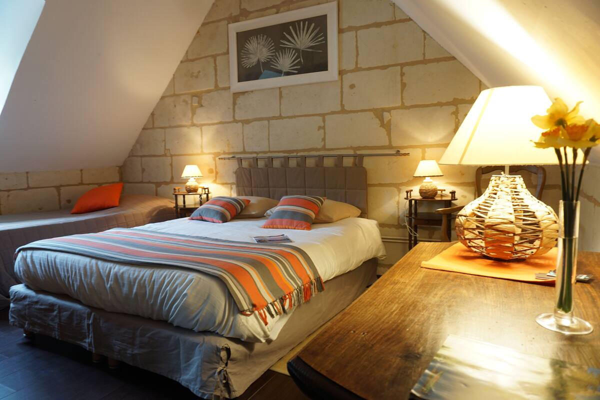 Une chambre confortable avec un plafond en pente, un grand lit avec une literie à rayures, deux lampes de chevet et une lampe décorative en osier posée sur la table de chevet.