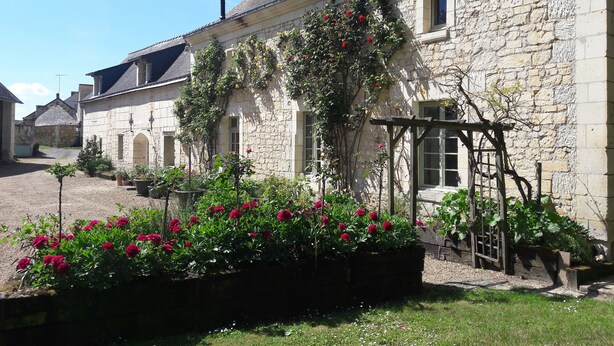 Un edificio de piedra con un jardín delantero, con flores rojas y plantas trepadoras.