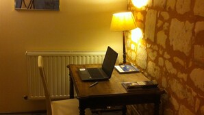 Una habitación con una mesa de madera, una computadora portátil, una lámpara, un radiador, una silla y un cuadro en la pared.