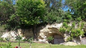 Un edificio de piedra con puerta de madera, rodeado de abundante vegetación y plantas con flores.