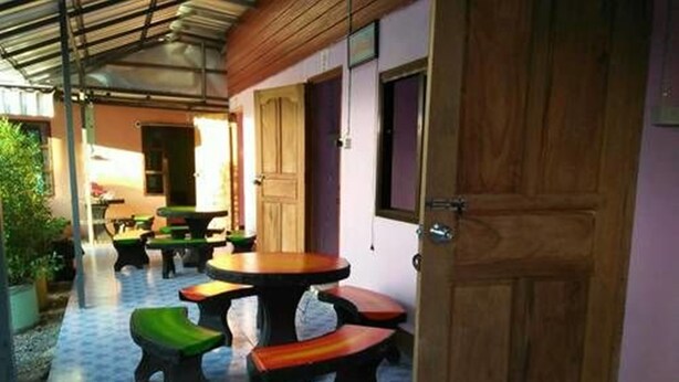 Uma área de estar coberta ao ar livre com mesas e bancos, uma porta de madeira e piso ladrilhado.