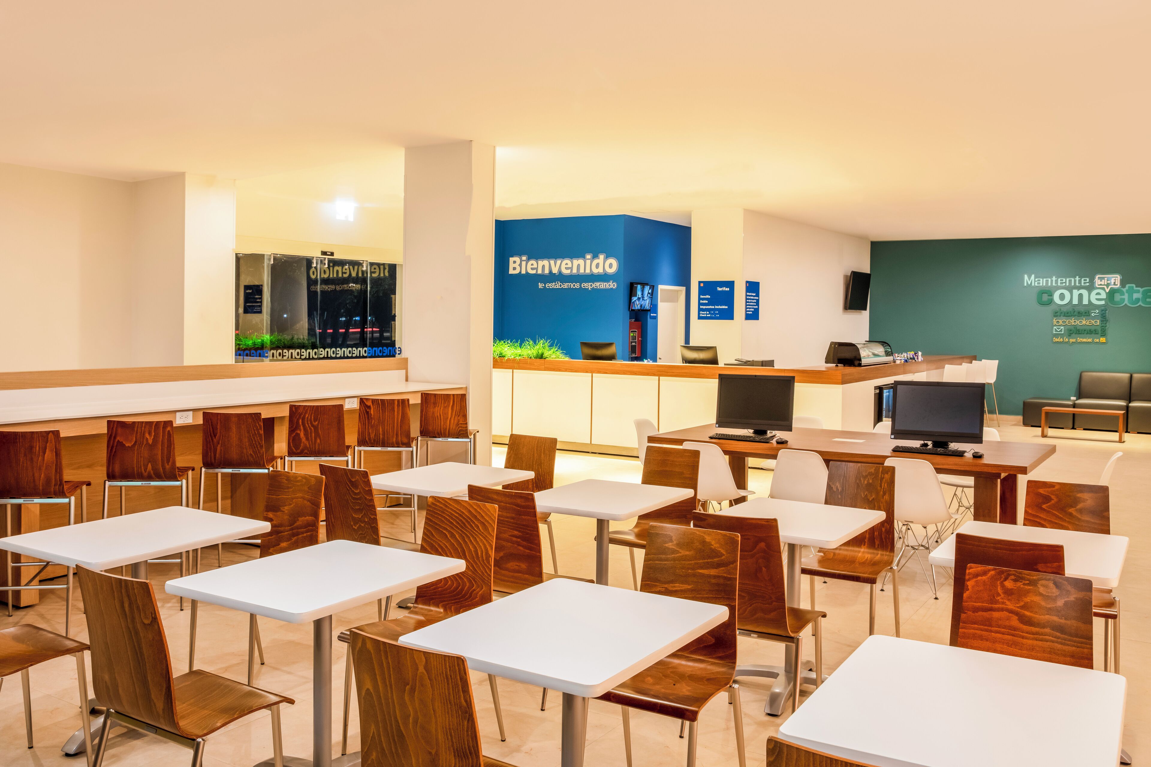 A hotel lobby with a reception desk, a TV, and a seating area with tables and chairs.