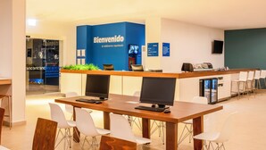 A modern reception area with a blue wall, a reception desk, multiple computer monitors, and white chairs. - One Ciudad de Mexico La Raza (Mexico City)