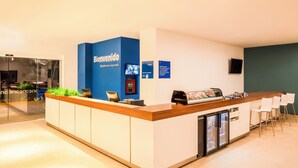 A reception area with a blue counter, a coffee machine, a refrigerator, and a seating area with white chairs. - One Ciudad de Mexico La Raza (Mexico City)