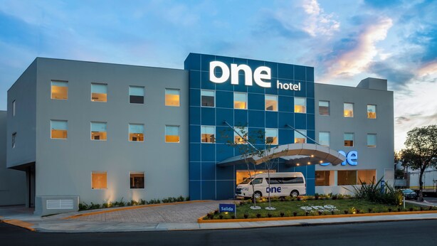 A modern hotel building with a prominent 'one hotel' sign, a van parked in front, and a well-maintained garden area. - One Ciudad de Mexico La Raza (Mexico City)