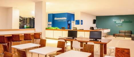 A modern hotel lobby with a reception desk, seating area, and a large screen.