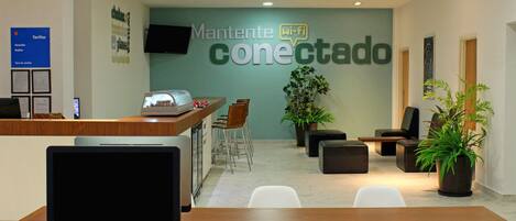 Zona de recepción con mostrador, computadora y asientos. Un cartel dice 'Mantente conectado'.