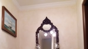 Un pasillo con un espejo decorativo, una mesita con un florero y un piso de baldosas.