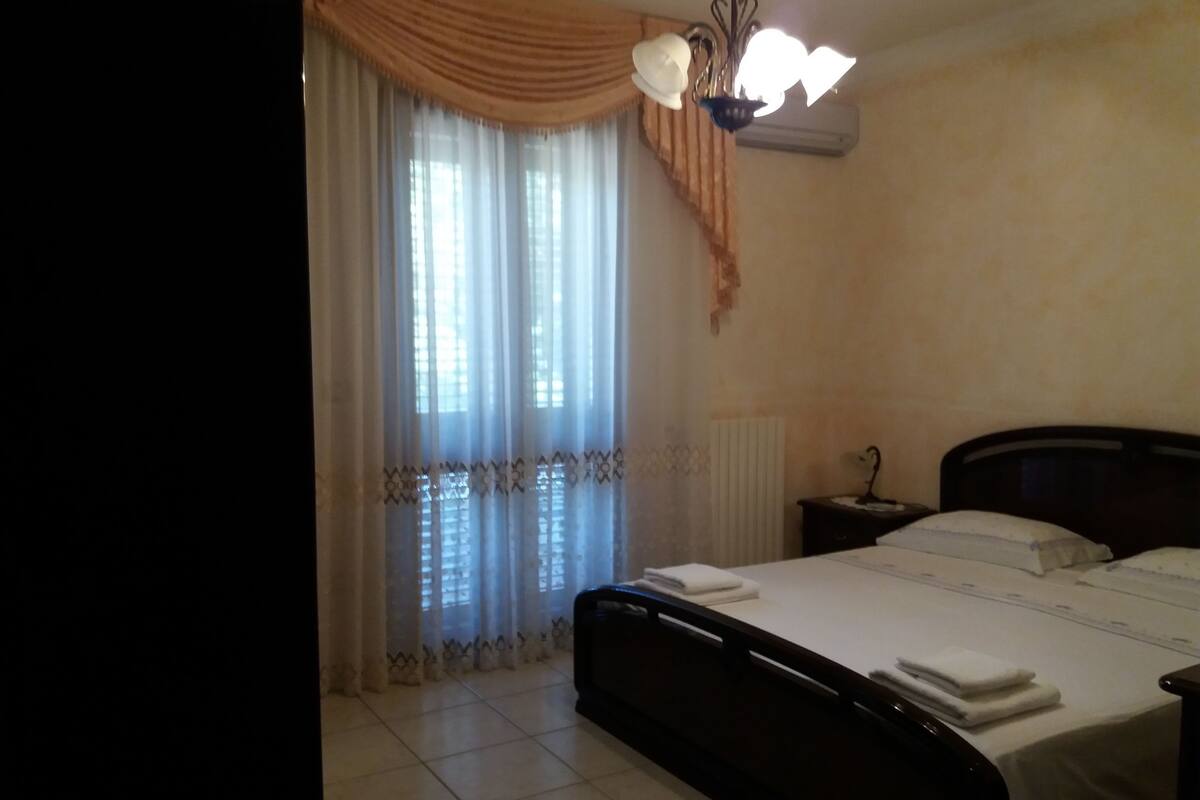 Un dormitorio con cama, mesita de noche, lámpara y ventana con cortinas.