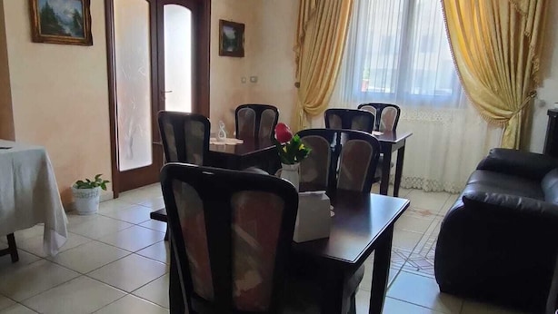 Un comedor con una mesa, sillas, un sofá, una araña y cortinas.
