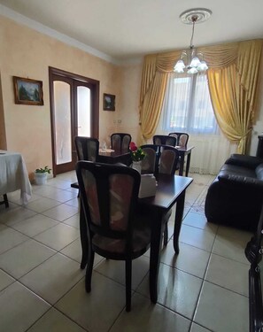 Un comedor con una mesa, sillas, un sofá, una araña y cortinas.