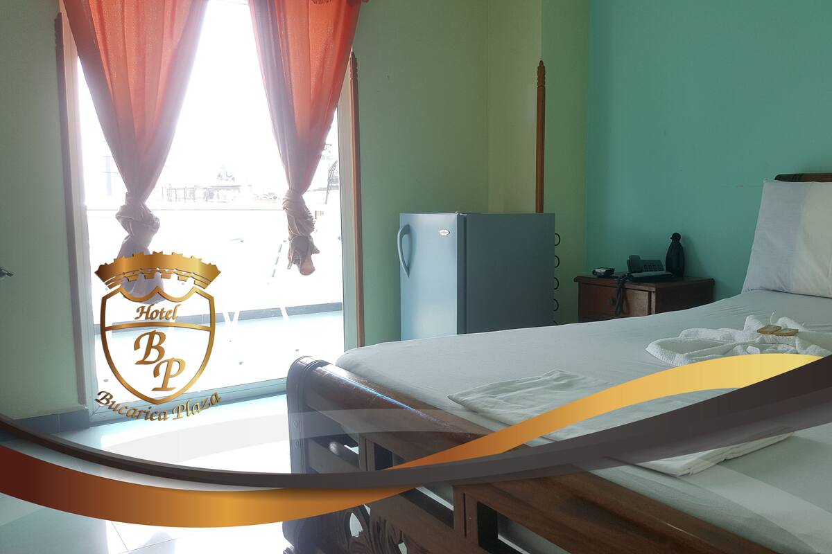 A hotel room with a bed, a nightstand, a refrigerator, and a window with curtains.