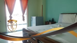 Habitación de hotel con cama, mesita de noche, refrigerador y ventana con cortinas.